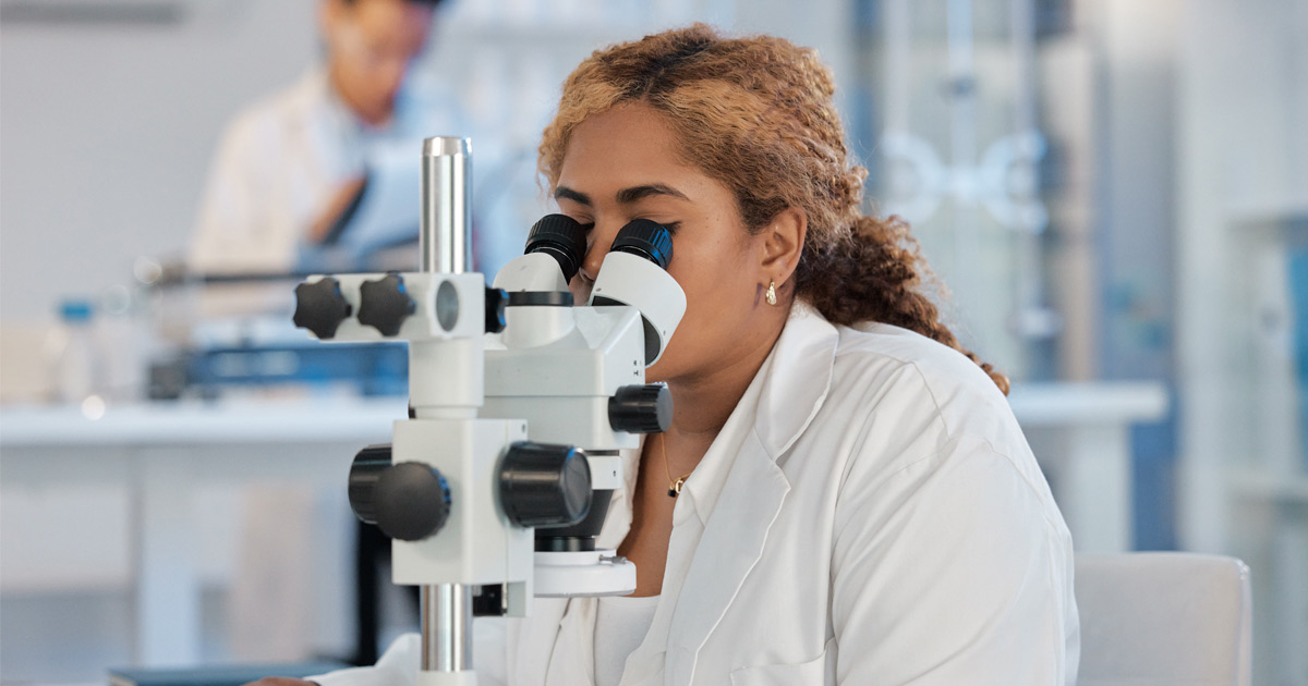 A researcher looks through a microscope in a lab.