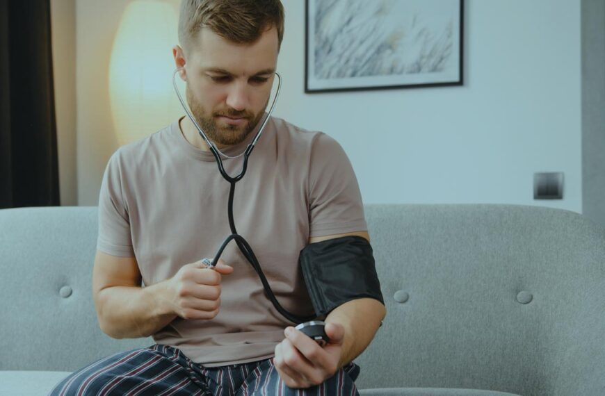 A man sits on the couch in his pajamas and gives himself a blood pressure check.
