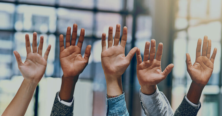 A close up of a bunch of hands being held up in a "count me in" kind of gesture.