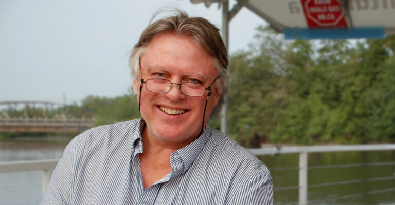 Jim Wilson under an awning on a river side, smiling widely.
