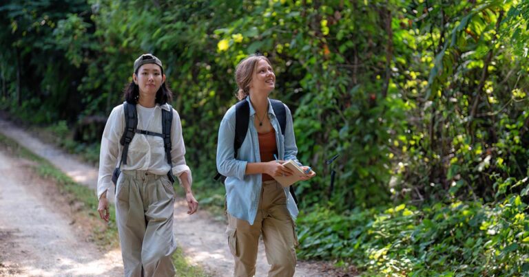 Two young people go hiking and wear long pants that are light coloured.