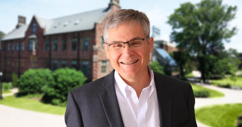 Mount Allison campus stretches across the background on a summer day, with Mario Levesque smiling happily in the foreground.