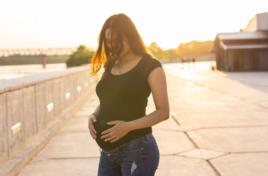 A woman stands in a courtyard, pregnant, happy in the glowing light of the late afternoon.
