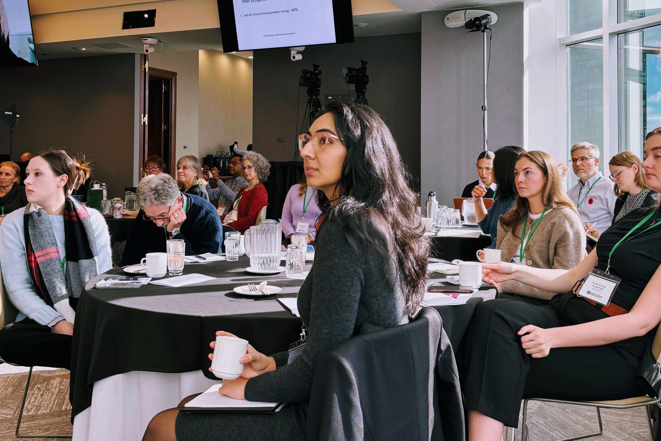 Conference attendees sit at their tables during a presentation in a beautiful room and venue.
