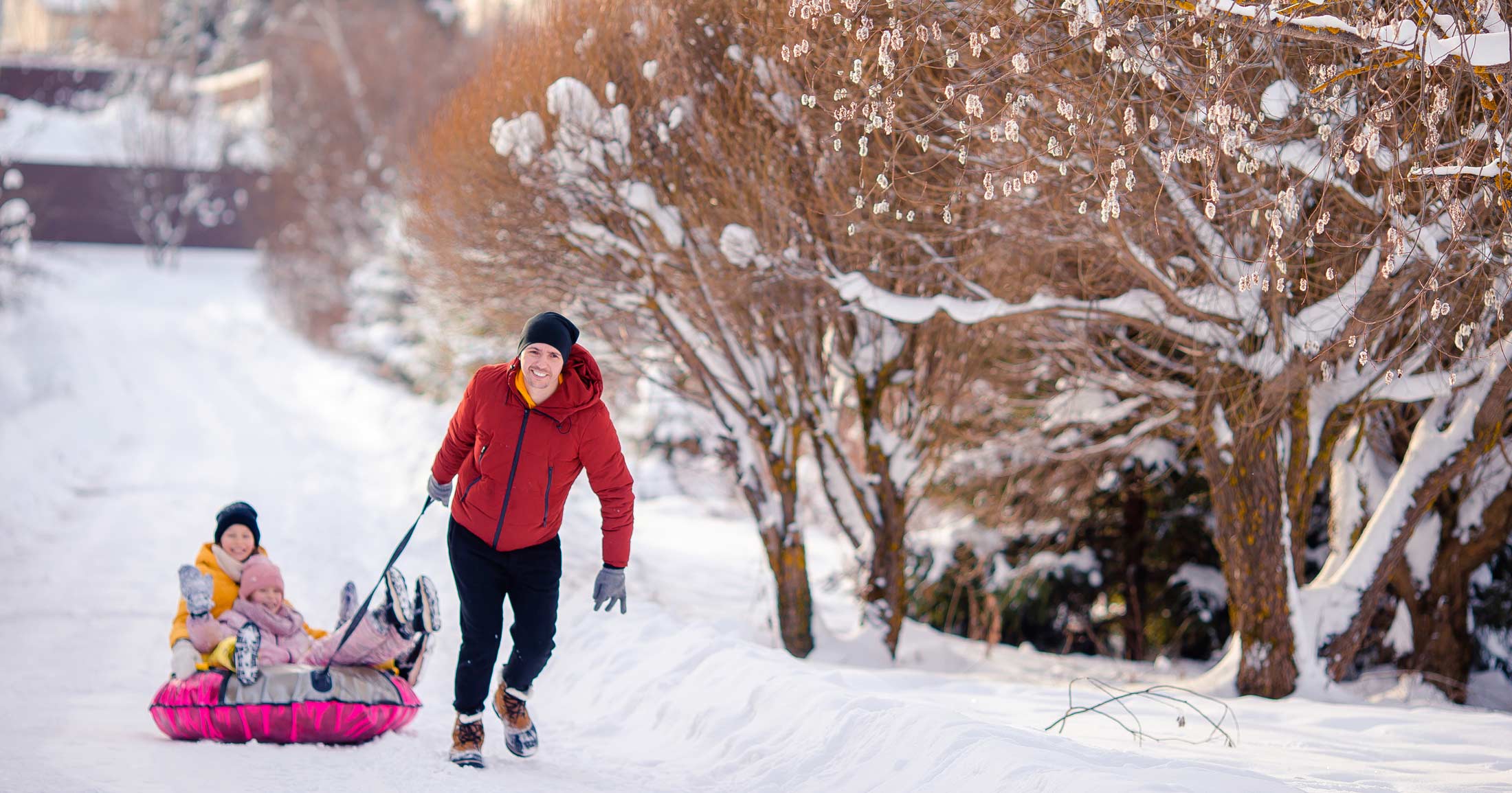 A parent hauls their two kids up a snowy slope in a sled and everyone is still smiling.