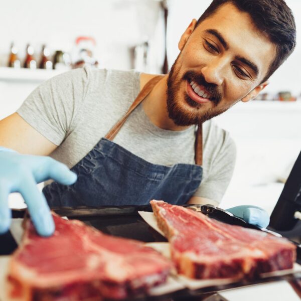A butcher smiles while showing off some steaks over a counter.
