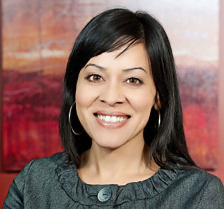 Dr. Aparna Taylor smiles warmly with a bright red background and long dark hair.