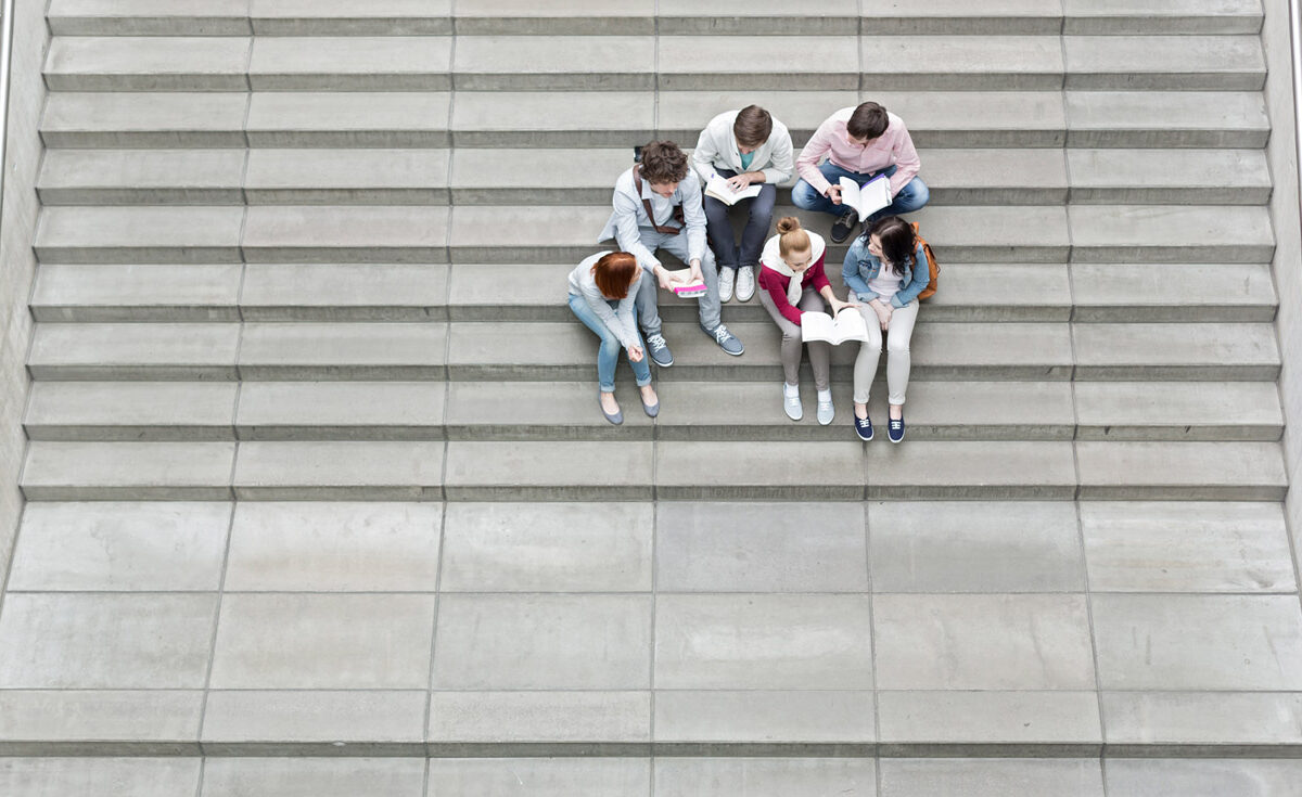 Aerial view of a small group of students or youth sitting on large wide concrete stairs, studying and looking at their books.