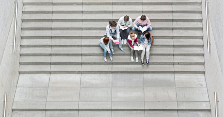 Aerial view of a small group of students or youth sitting on large wide concrete stairs, studying and looking at their books.