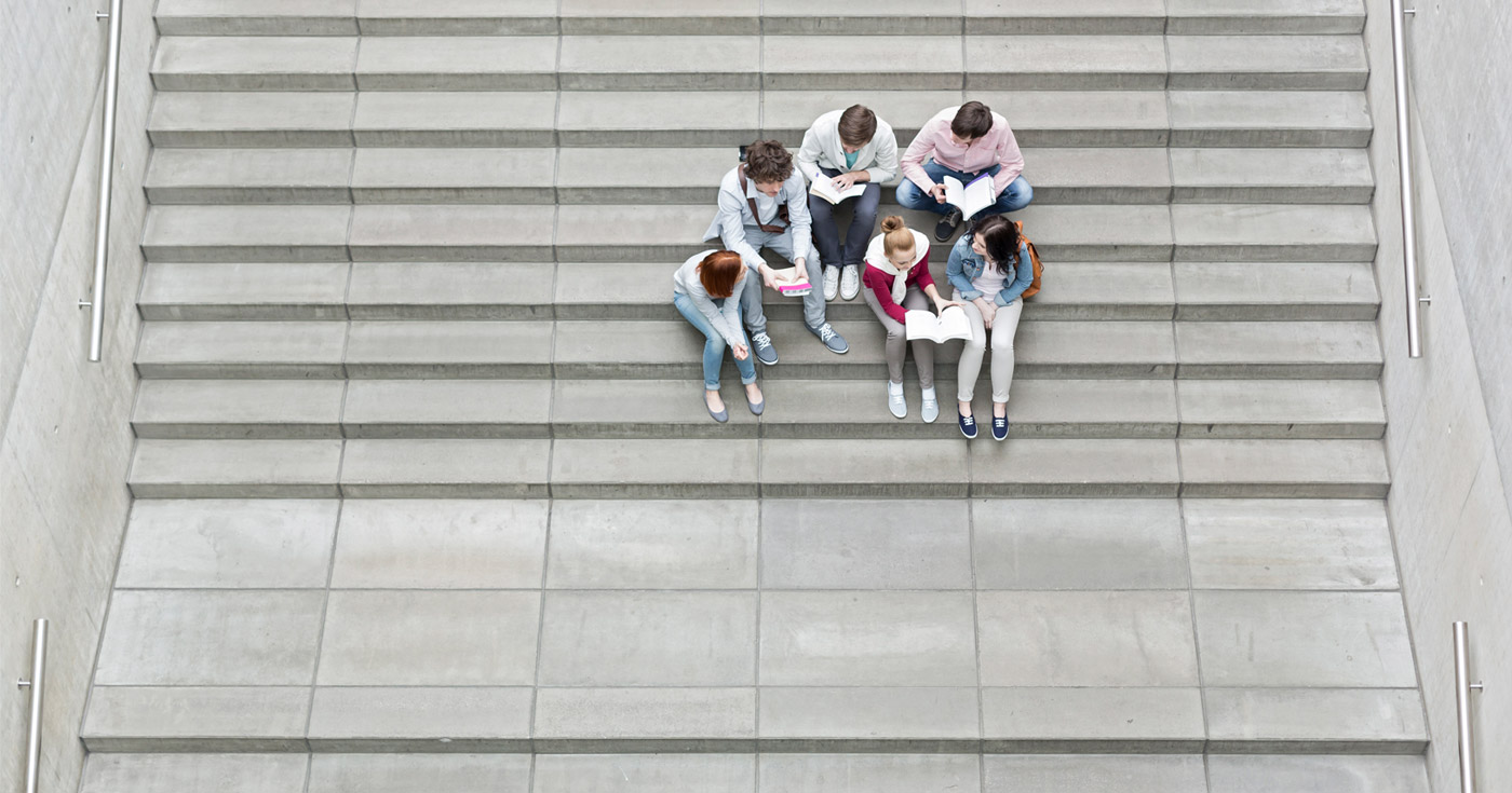 Aerial view of a small group of students or youth sitting on large wide concrete stairs, studying and looking at their books.